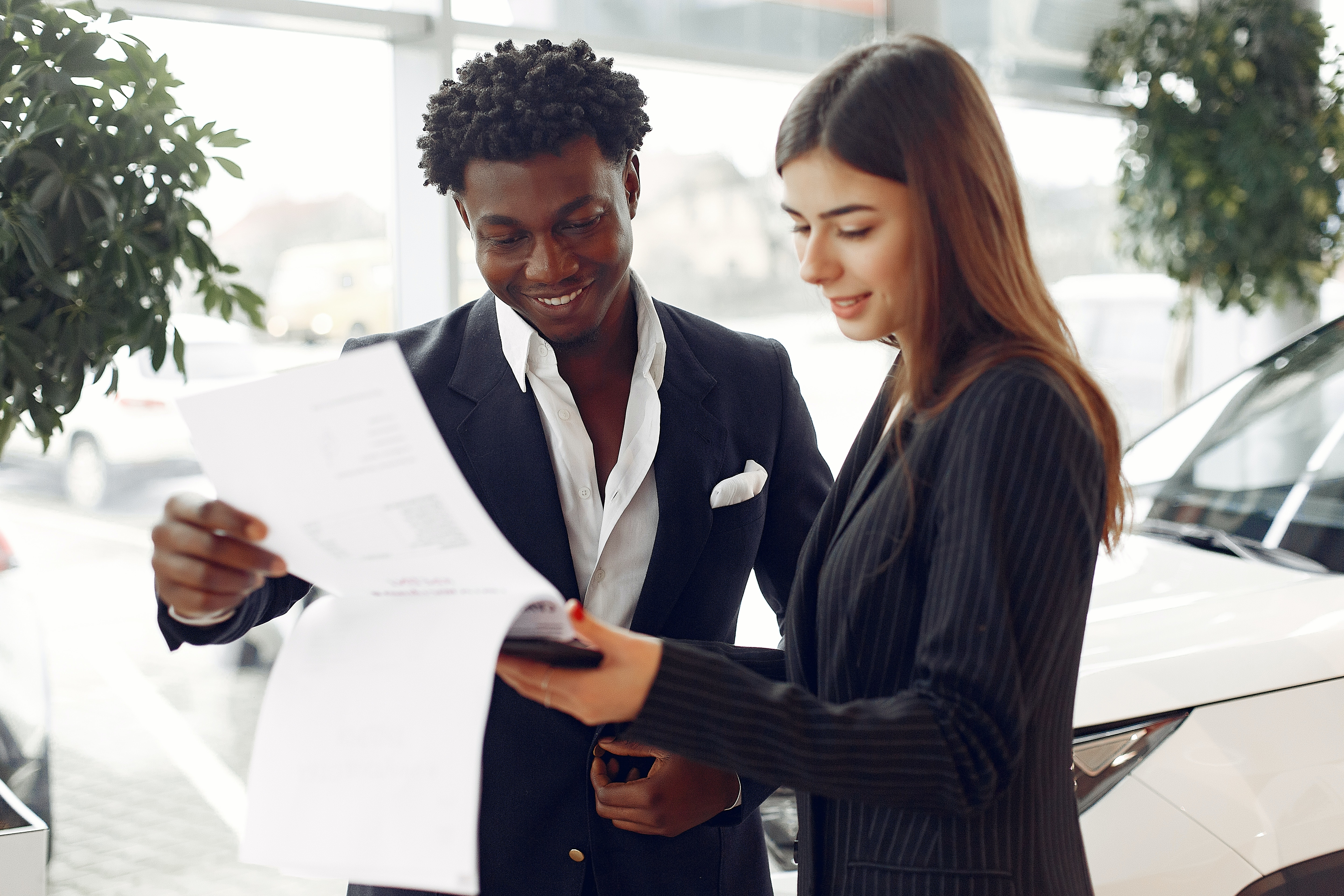 Two smiling people flip through the pages of a contract in a car dealership.